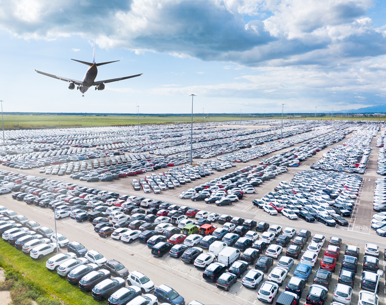 Großes Flughafen-Parkhaus mit hunderten geparkten Autos und landendem Flugzeug – ETI Experts Köln bietet effizientes Parkraummanagement für Parkhäuser und Flughäfen.